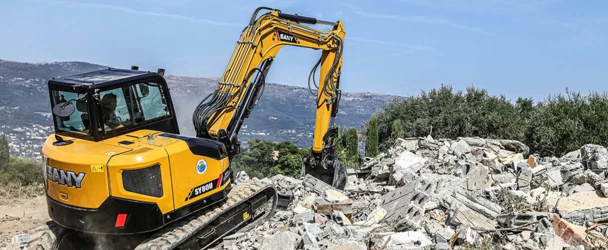 Koparka SANY SY80U pracuje przy usuwaniu gruzu na tle górzystego krajobrazu.
