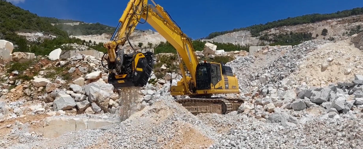 Koparka z przesiewaczem bębnowym przetwarza urobek skalny w kamieniołomie na tle skalnego zbocza.