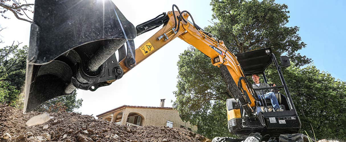 Operator koparki wykonuje wykop przy domu jednorodzinnym w słoneczny dzień