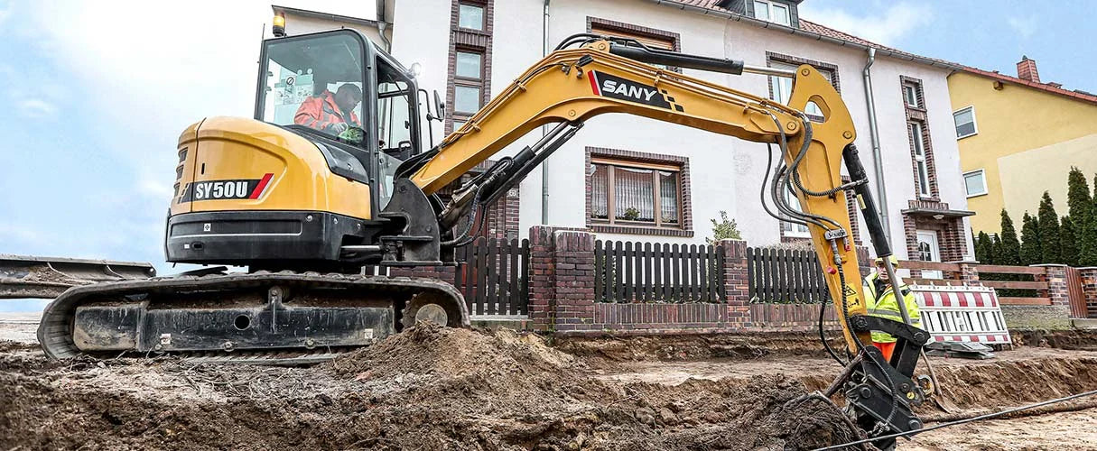 Minikoparka SANY SY50U prowadzi wykopy wzdłuż ogrodzenia domu jednorodzinnego.