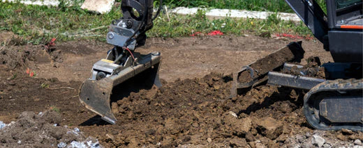 Minikoparka wykonuje wyrównanie gruntu w miejscu przygotowanym pod budowę. Maszyna pracuje na otwartym terenie z widoczną warstwą urobku ziemnego.