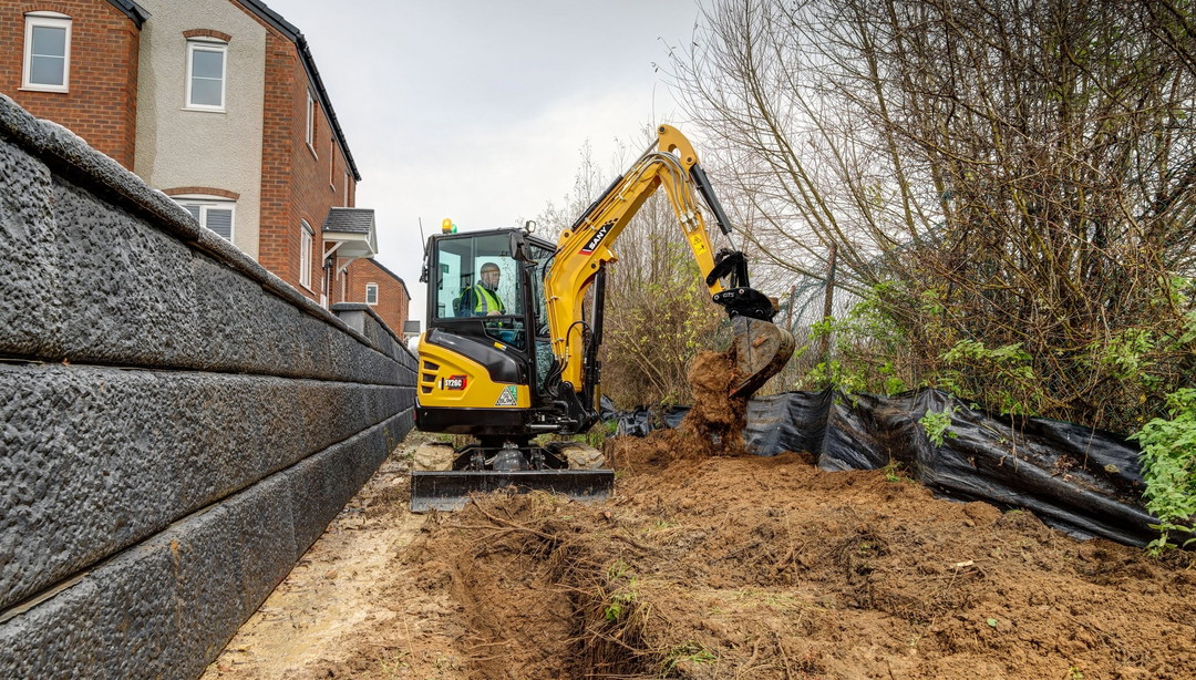 Minikoparka zeroobrysowa przy murze, wykonująca prace wykopkowe.