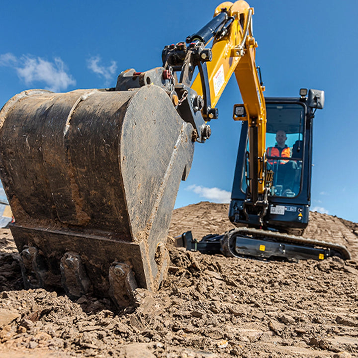 W centrum łyżka podsiębierna na tle operator sterujący minikoparką.
