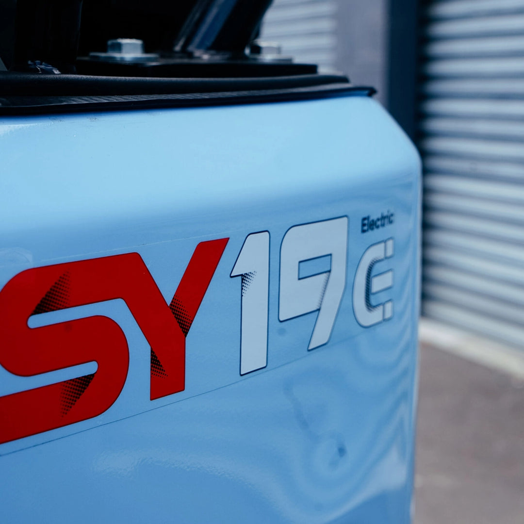Zbliżenie na logo i oznaczenie modelu SY19E Electric na obudowie niebieskiej minikoparki Sany.