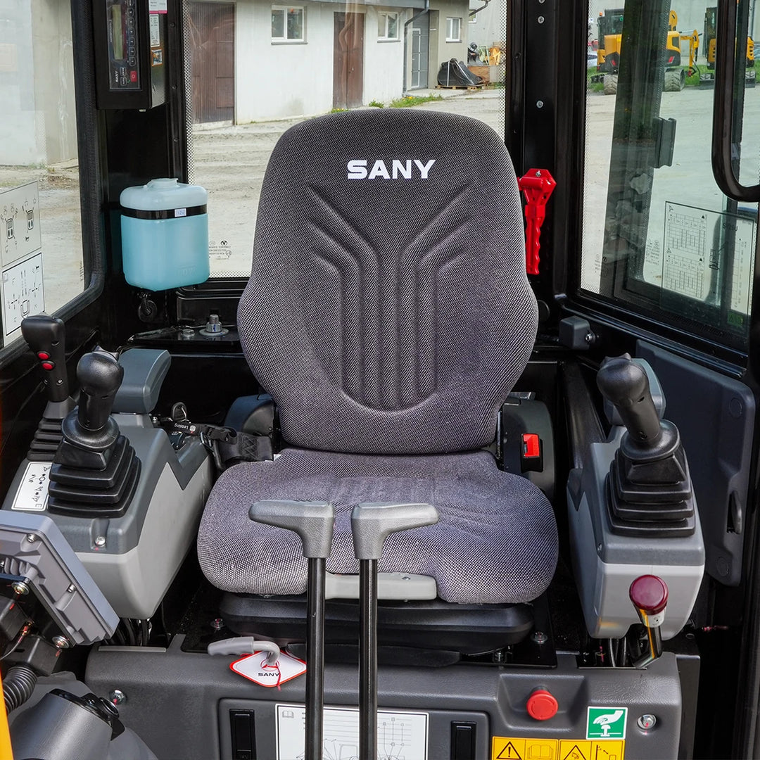 Wnętrze kabiny mini-koparki Sany SY26U; widok na ergonomiczny fotel operatora z logo SANY oraz precyzyjne joysticki sterujące.