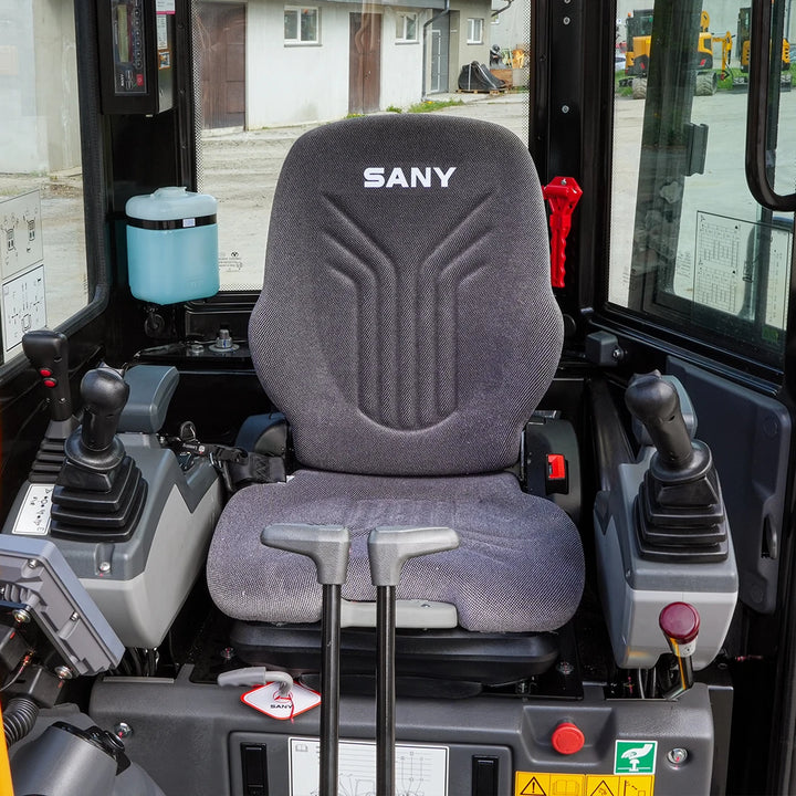 Wnętrze kabiny mini-koparki Sany SY26U; widok na ergonomiczny fotel operatora z logo SANY oraz precyzyjne joysticki sterujące.