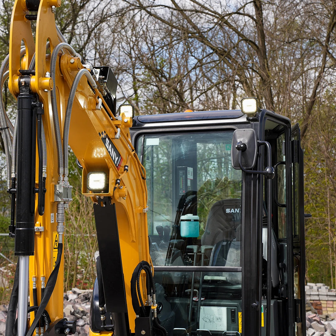 Sany SY26U - detale ramienia koparki: zabezpieczone linie hydrauliczne, logo SANY oraz wytrzymały mechanizm wysięgnika na tle drzew.
