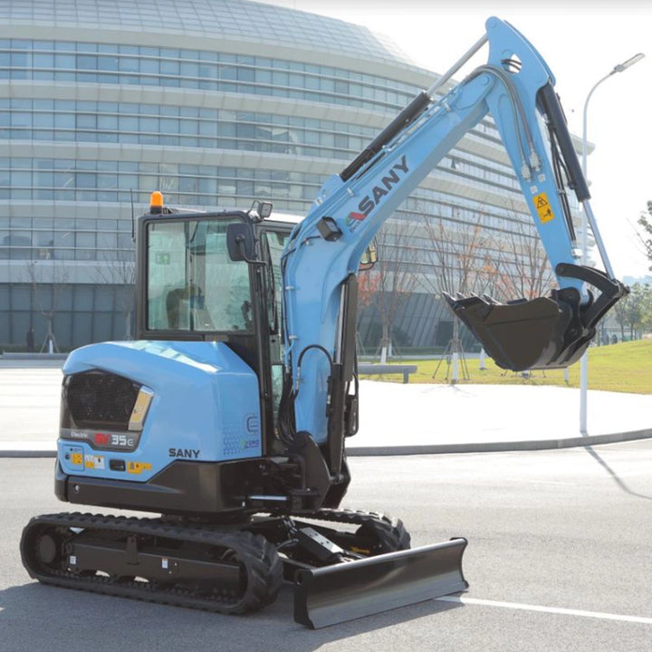 Mini-koparka elektryczna Sany SY35E z uniesionym ramieniem i opuszczonym lemieszem na tle biurowca.