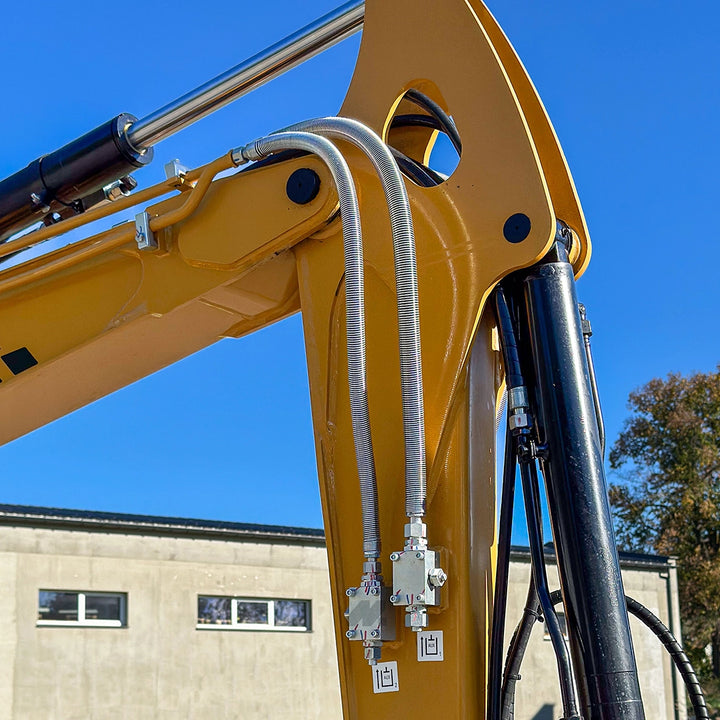 Zbliżenie na ramię minikoparki Sany SY35U: widoczne przewody hydrauliczne w stalowym oplocie i siłownik na tle błękitnego nieba.