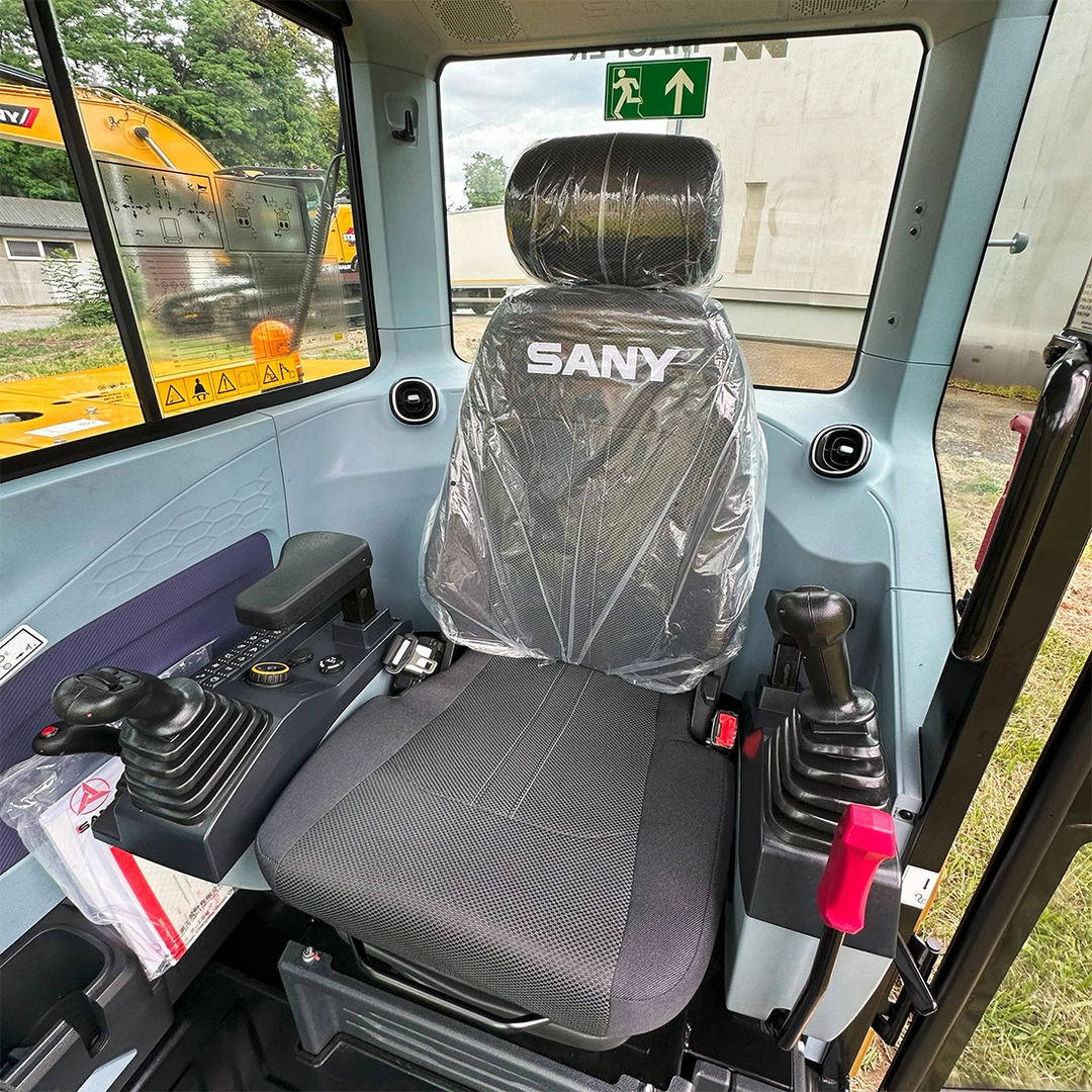 Wnętrze kabiny operatora minikoparki Sany SY60U z regulowanym fotelem z logo producenta i ergonomicznymi joystickami sterującymi.