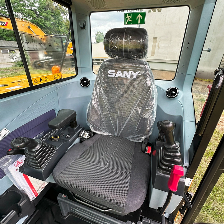 Wnętrze kabiny operatora minikoparki Sany SY60U z regulowanym fotelem z logo producenta i ergonomicznymi joystickami sterującymi.